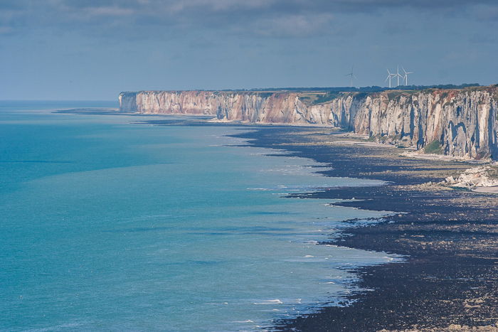 High point of view photo of a cliff side in the horizon against a blue sea and clear blue sky