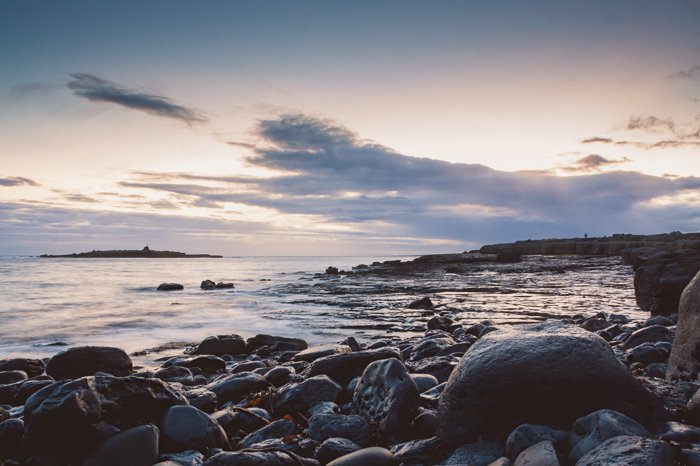 Foto de punto de vista bajo de rocas en la costa al amanecer contra un amanecer nublado y suave