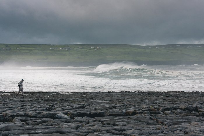 Una silueta solitaria de un hombre caminando por una playa con grandes olas detrás de él.