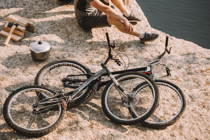 Cropped photo composition of a man sitting on rocks beside two bicycles