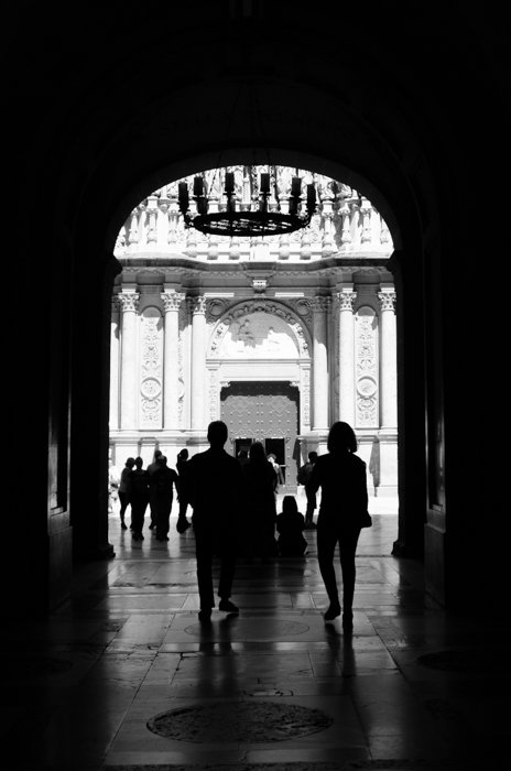 A black and white street image of people walking under an archway