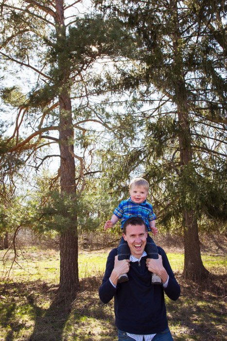 A portrait of a father holding his young son on his shoulders in a forest area 