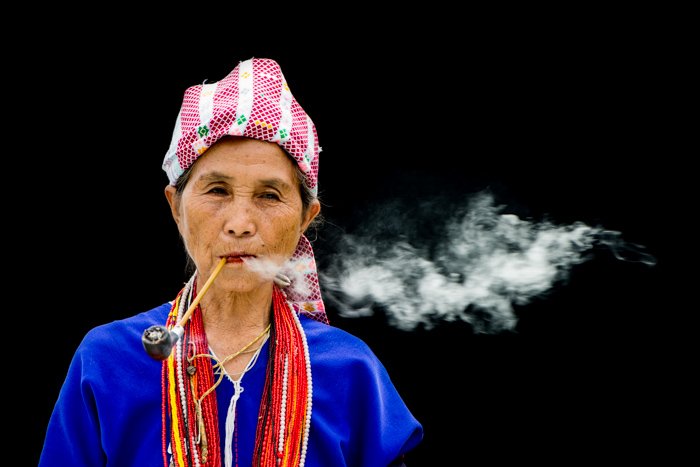 A Karen Woman Smoking a pipe against a black background - figure to ground photography composition
