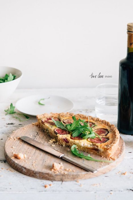 half pizza on a wooden tray on a white table with herbs on top beside a knife, a bottle of wine on the table