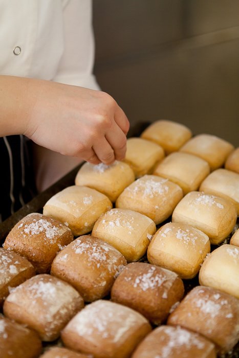 close up of baker's hand sprinkling sugar on newly baked buns