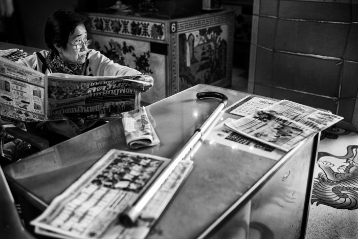 black and white portrait of a woman reading a newspaper at a table 