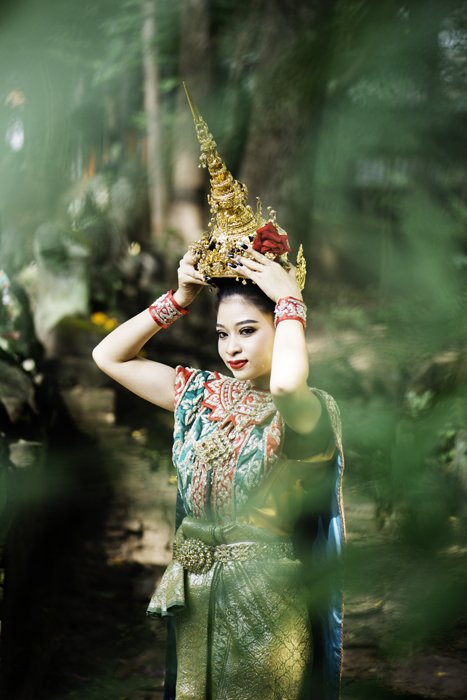 A photo of a Thai woman in traditional costume framed by a tree in the foreground.
