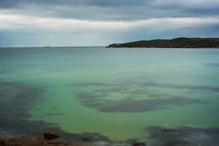 sea green and cloudy skies, a small mountain on the horizon