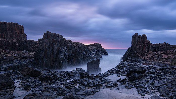 rocky sea shore, outcropping into foamy foggy sea, cloudy blue and pink sky during sunrise