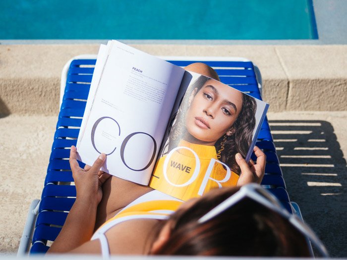 A girl reading a fashion magazine while sunbathing on a deck chair - magazine photographer tips