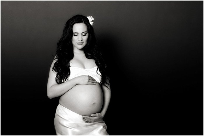 Pregnant woman wearing white, a flower in her hair, cradling her belly