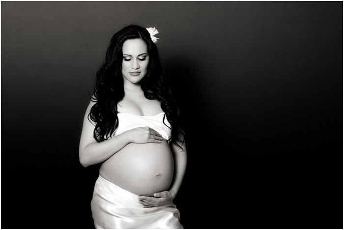 Pregnant woman wearing white, a flower in her hair, cradling her belly