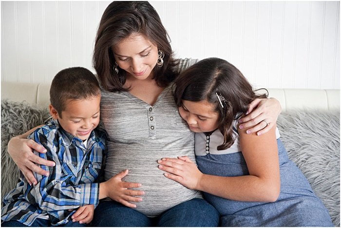 Beautiful maternity photography shot of a two children, boy and girl, looking and touching pregnant mom's belly