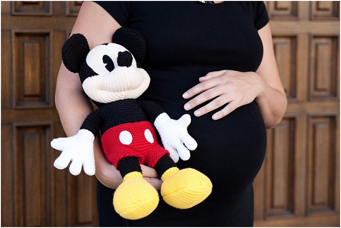close up pregnant woman holding her belly, holding a mickey mouse stuffed toy next to her