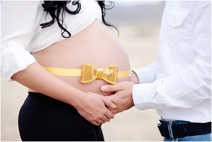 A close up of a man cradling pregnant wife's belly in his hands, a bright yellow and gold ribbon on her belly