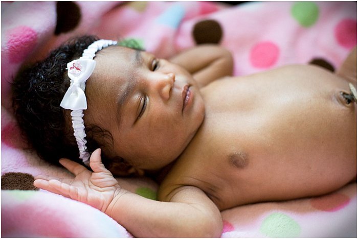 close up of newborn baby girl wearing a white headband sleeping on a pink blanket