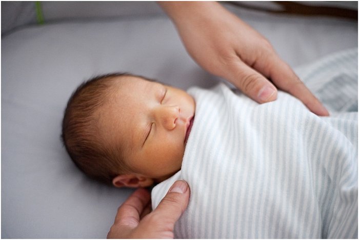 close up of baby wrapped up and sleeping, with parents' hands on him during a newborn portrait session