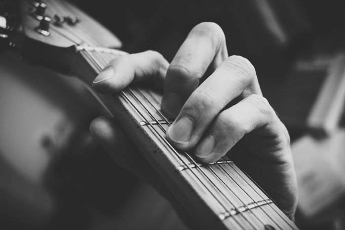 A close up black and white photo of a persons hand playing guitar