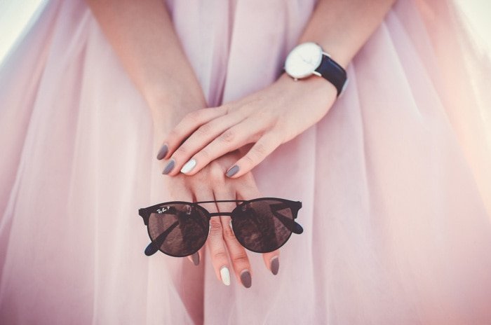 close up of a model in a pink dress holding a pair of sunglasses 
