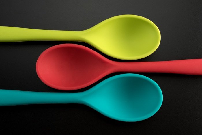 flat lay product photography shot of three colored spoons against a grey background 