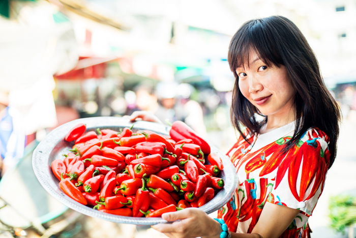 Young pretty Asian woman at an outdoor market with chili peppers. - photography props