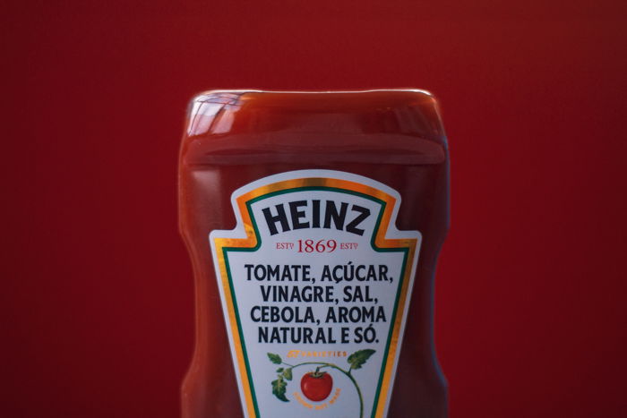 close up of half of heinz ketchuo bottle against matching dark red background