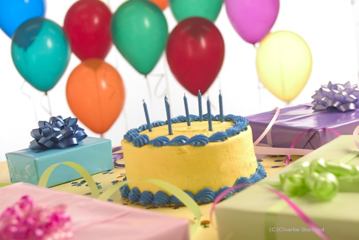 Still life product shot of a birthday cake, balloons, birthday presents wrapped in different colored paper and party streamers