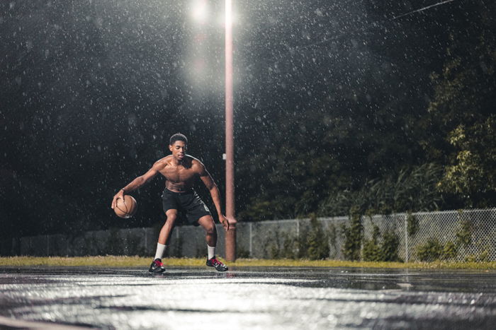 Atmospheric rain photo of a man playing basketball at night under lamp post light