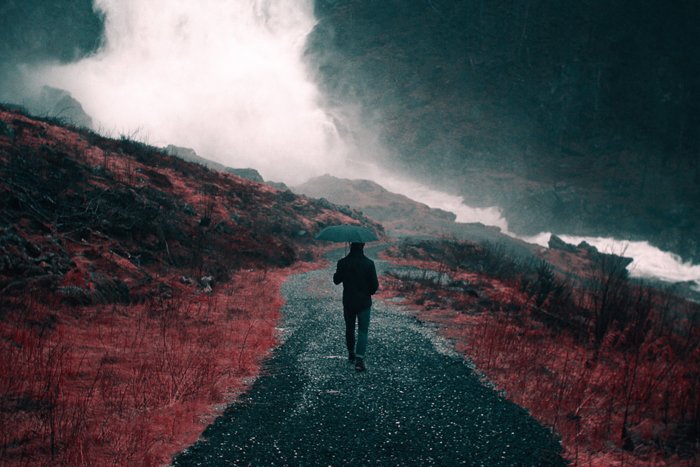 Dark and moody rain image of a person walking through a landscape with an umbrella