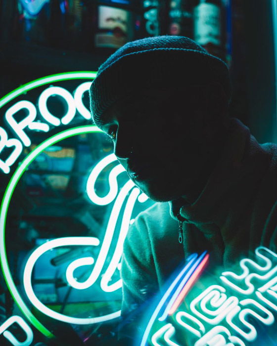 Low light portrait of a man posing in front of a neon sign at night