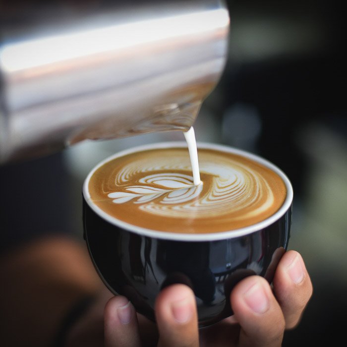 A smartphone food photography shot of a person pouring milk into a coffee