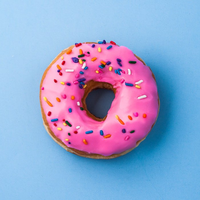A close up overhead shot of a pink iced doughnut on light blue background