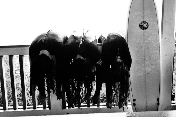 三名冲浪者靠在围栏上的黑白照片，一个冲浪板靠在围栏上——智能手机拍摄风格