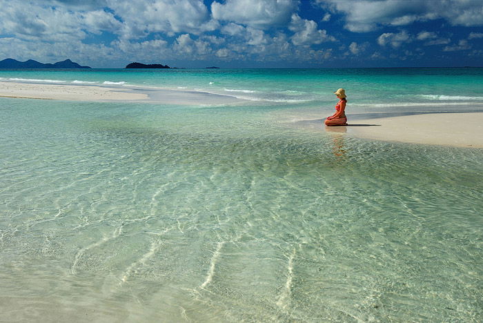 A woman sitting on the shore of a beautiful beach, shot using top lighting