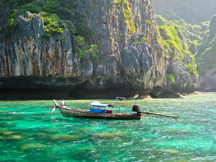 wooden boat on crystal blue green waters in Thailand