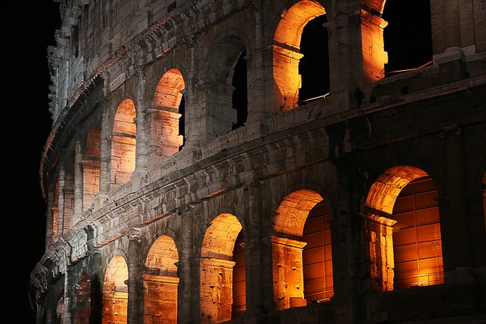 the Colosseum in Italy, lit from within with a warm orange yellow light, glowing in the night