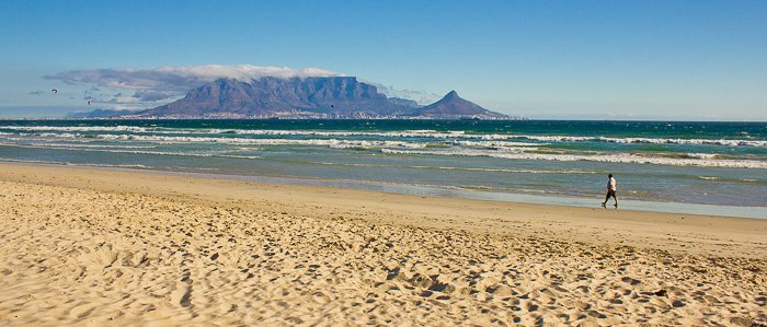 a man walking along the shore at a beach in Cape Town