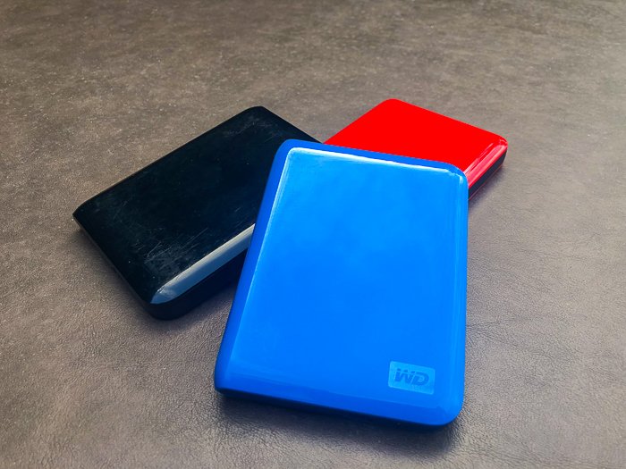 three external hard disk drives on a grey surface - travel safety tips for photographers