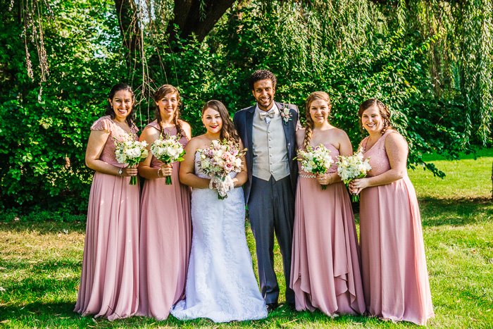 HDR photo of wedding entourage outdoors against bright trees, bride, groom, and bridesmaids in pale pink