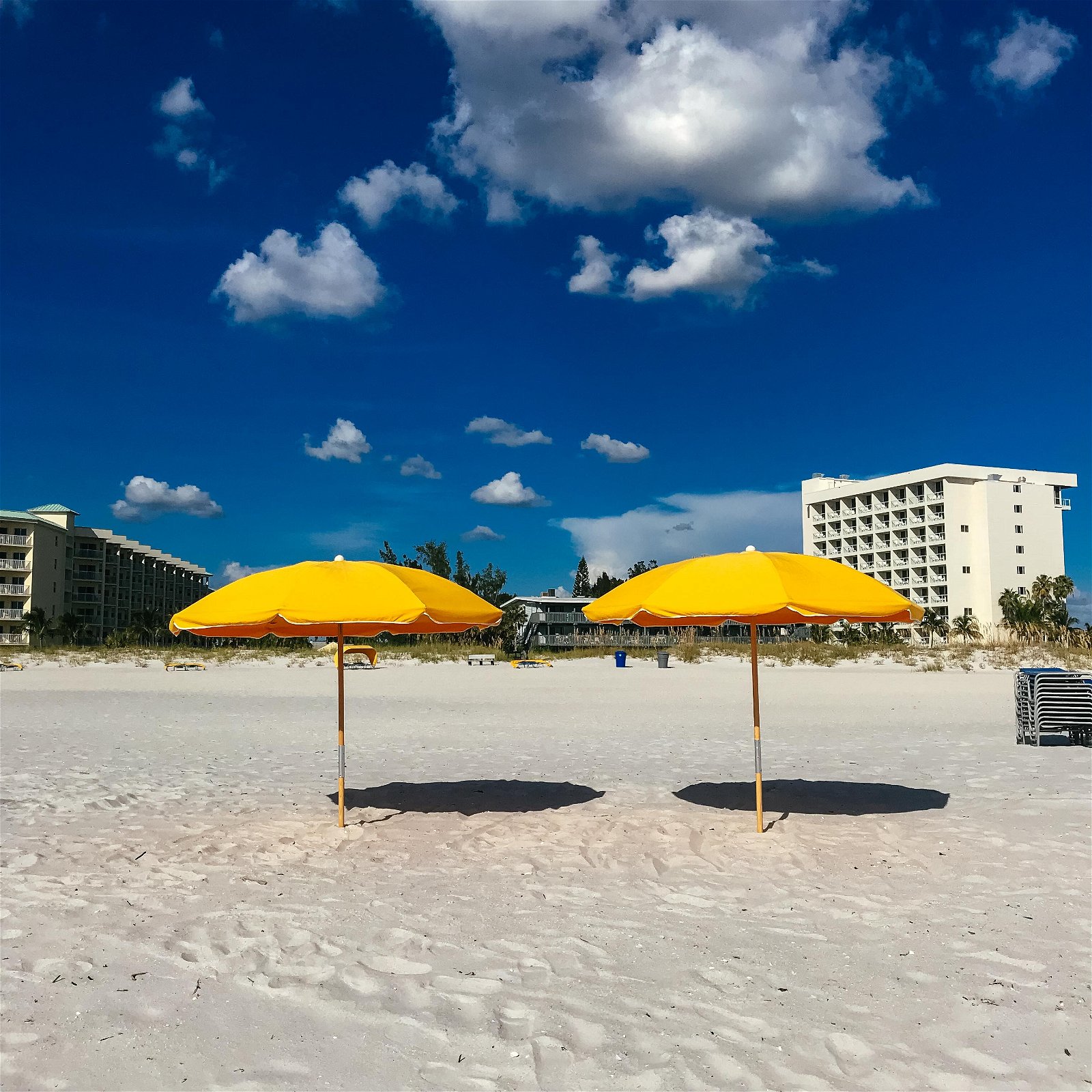 Two yellow umbrellas on a beach with white fluffy clouds in a blue sky