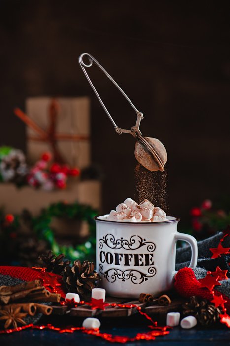 A magical Christmas still life photography shot of a coffee cup of marshmallows and levitating chocolate sprinkler