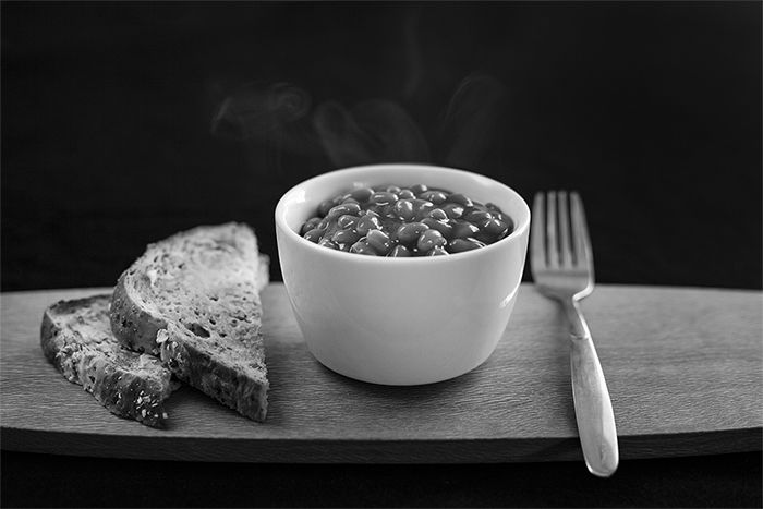 A black and white food photography shot of baked beans and bread on a wooden tray