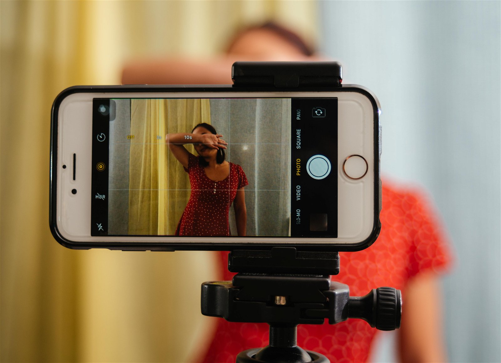 Close-up of an iPhone on a tripod mount with the native camera app open to take a picture of a woman in a red dress with her hand covering her face