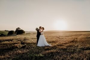Bride and groom kissing in a field at sunset