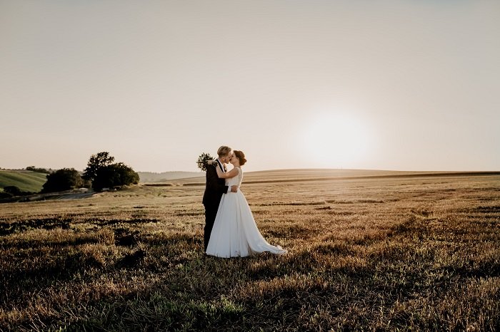 Noiva e noivo beijando em um campo ao pôr do sol