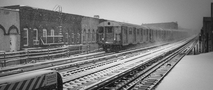 A black and white fine art photo of a train arriving at the platform in winter in Brooklyn, New York.