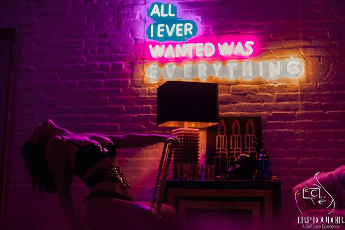 A boudoir photography model posing sensually indoors in front of a neon sign - tips for boudoir clients