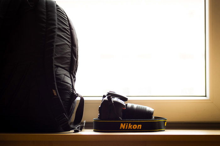 A Nikon camera placed on a shelf beside a camera backpack 