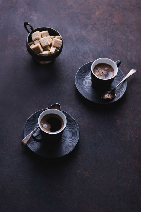 A dark and atmospheric fine art food photography still life featuring two coffee cups and sugar