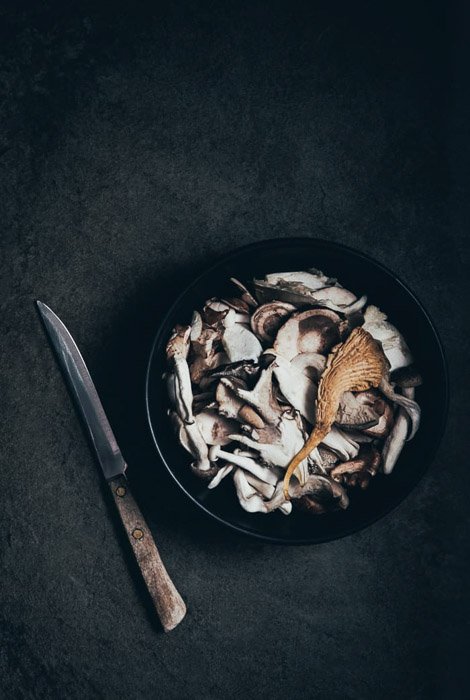 A dark and atmospheric fine art food photography still life ofmushrooms and a knife